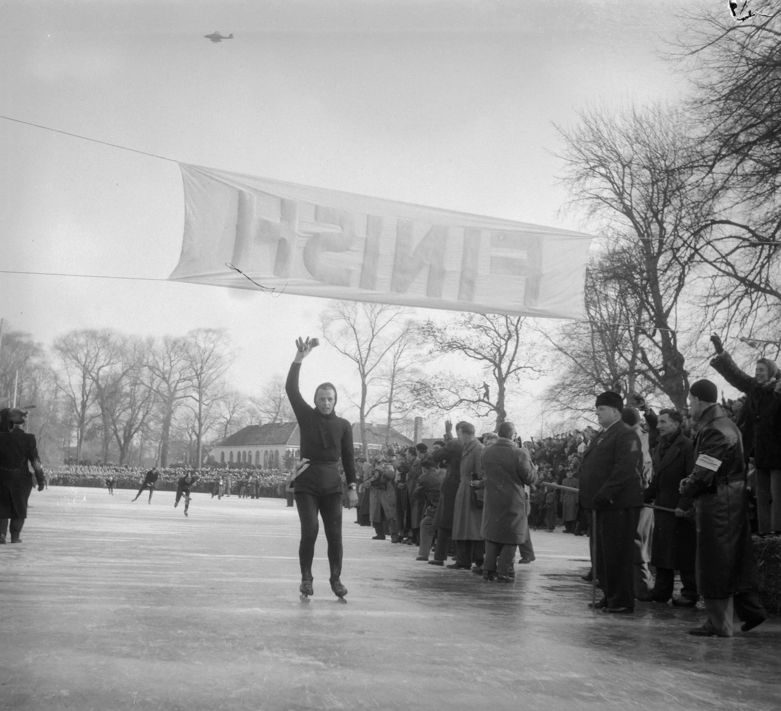 Jeen van den Berg uit Heerenveen passeert zwaaiend de finish in Leeuwarden tijdens de Elfstedentocht van 3 februari 1954