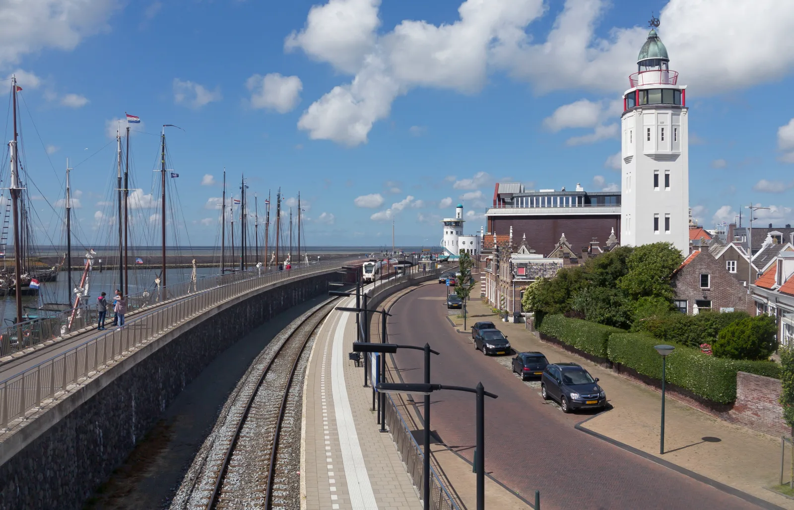 De witte vuurtoren van Harlingen aan de Waddenzee met op de voorgrond zeilschepen in de haven en de spoorbrug