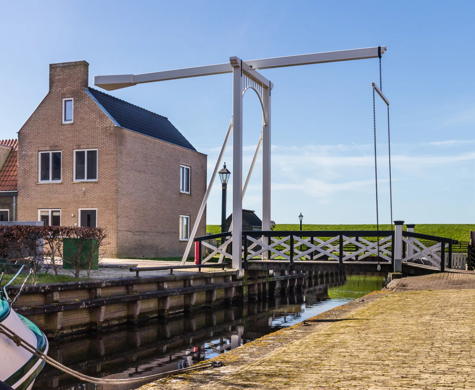 Witte ophaalbrug en Fries woonhuis in Hindeloopen onder blauwe lucht, sfeerbeeld van een traditioneel Fries stadje