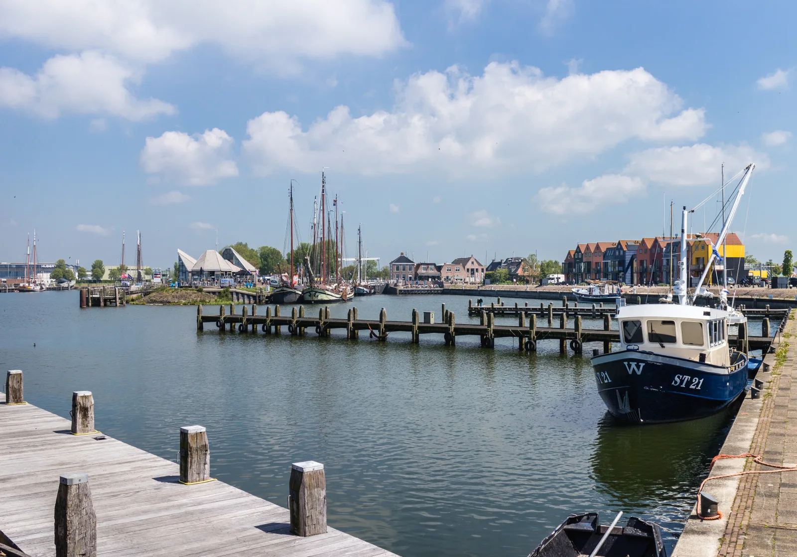 De haven van Stavoren aan het IJsselmeer met houten steigers, een vissersboot en zeilschepen onder een blauwe zomerlucht